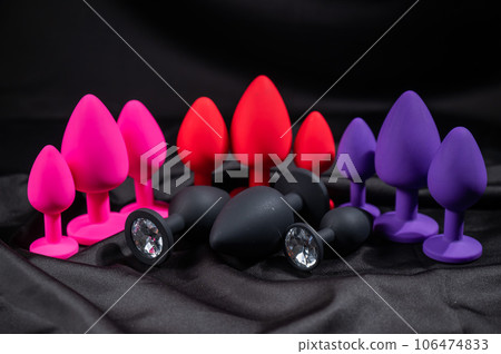 A set of silicone anal plugs in different colors and sizes on a black silk sheet.  106474833