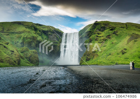 Powerful Skogafoss waterfall flowing with couple tourist enjoying in summer at Iceland Powerful Skogafoss waterfall flowing with couple tourist enjoying in summer at Iceland 106474986