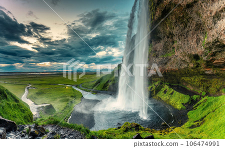 Beautiful Seljalandsfoss waterfall flowing and lush field on gloomy day in summer Beautiful Seljalandsfoss waterfall flowing and lush field on gloomy day in summer 106474991