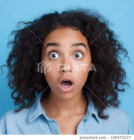 Portrait of a surprised Latin American woman with big eyes and an open mouth. Closeup face of an amazed adult Latin girl on a blue background. Astonished grownup in a blue shirt looking at the camera. Portrait of a surprised Latin American woman with big eyes and an open mouth. Closeup face of an amazed adult Latin girl on a blue background. Astonished grownup in a blue shirt looking at the camera. 106475037