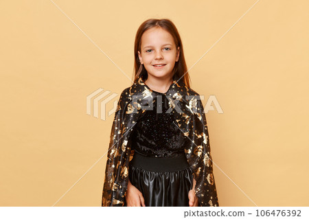 Cute charming smiling little girl wearing witch costume isolated over beige background looking at camera celebrating halloween having fun at theme party. 106476392