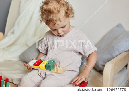 Wooden construction set. Active toddler play. Creative learning games. Cognitive skill development. Little blonde baby girl palying with wooden sorter toys at home interior. Wooden construction set. Active toddler play. Creative learning games. Cognitive skill development. Little blonde baby girl palying with wooden sorter toys at home interior. 106476778