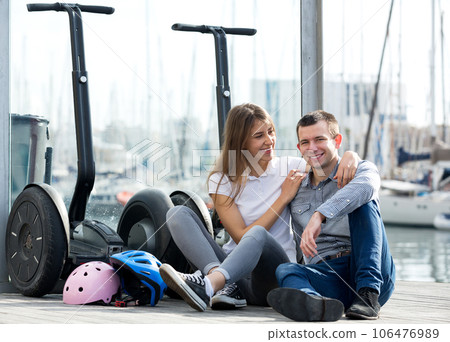 Couple sitting near segways at sea front Couple sitting near segways at sea front 106476989