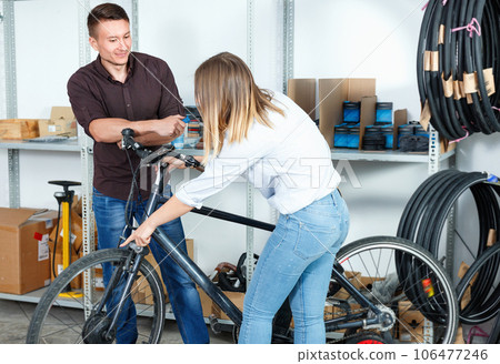 Man with woman are lubricating the bicycle mechanism with silicone in the workshop. 106477246