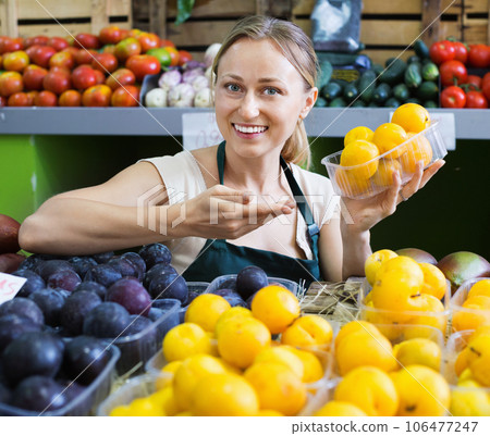 Cheerful female seller wearing apron holding plums 106477247