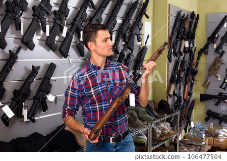 Guy choosing air rifle in military store 106477504