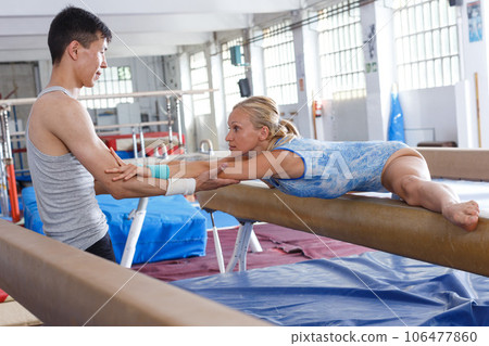 Woman in bodysuit training at broad bars in sport gym, man helping 106477860
