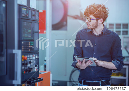 Professional young engineer factory worker programming CNC milling machine with a tablet computer. 106478387