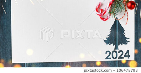 Christmas 2024 background. White paper with fir-tree shape cut for new year 2024 card on wooden table Christmas 2024 background. White paper with fir-tree shape cut for new year 2024 card on wooden table 106478798