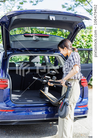 A woman putting an electric scooter on a car A woman putting an electric scooter on a car 106479402