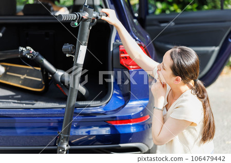 A woman putting an electric scooter on a car A woman putting an electric scooter on a car 106479442