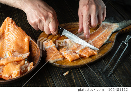 Close-up of a chef's hands with knives while cutting fresh fish on a cutting kitchen board before preparing herring 106481112