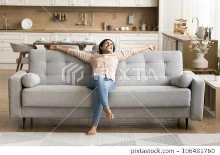 Cheerful positive Indian new homeowner stretching body on couch Cheerful positive Indian new homeowner stretching body on couch 106481760