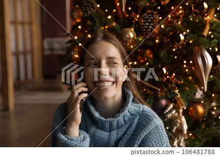 Happy young woman holding phone call, sitting near Christmas tree. Happy young woman holding phone call, sitting near Christmas tree. 106481788