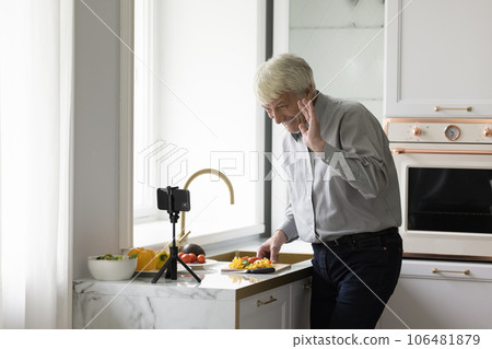 Cheerful happy mature chef blogger man filming cooking on smartphone Cheerful happy mature chef blogger man filming cooking on smartphone 106481879