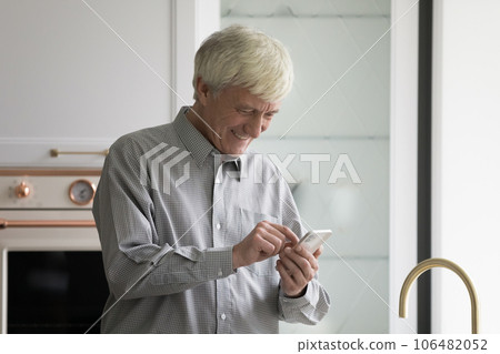 Cheerful mature retired man using smartphone in kitchen Cheerful mature retired man using smartphone in kitchen 106482052
