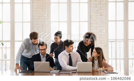 Smiling multiracial employees cooperate using laptops in office Smiling multiracial employees cooperate using laptops in office 106482086