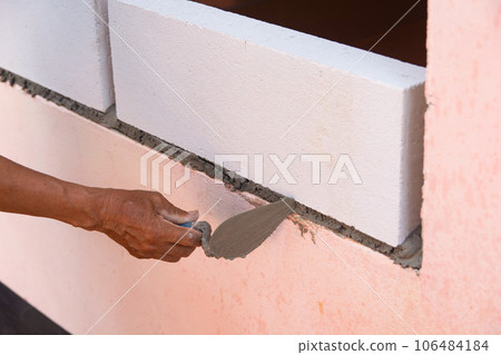 Bricklayer worker installing Lightweight Concrete on exterior wall with trowel putty knife. 106484184