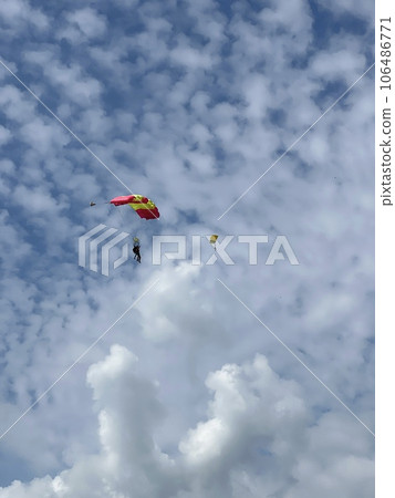 Skydiver with a blue little canopy of a parachute on the background a blue sky and white clouds, close-up. Skydiver under parachute above the stormy clouds. Lithuania 106486771