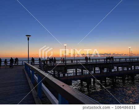 Palanga pier bridge with people resting against the background of the sea sunset Palanga pier bridge with people resting against the background of the sea sunset 106486831