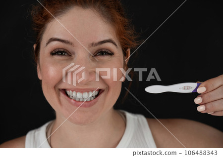 Portrait of happy caucasian woman holding positive express pregnancy test on black background. Portrait of happy caucasian woman holding positive express pregnancy test on black background. 106488343