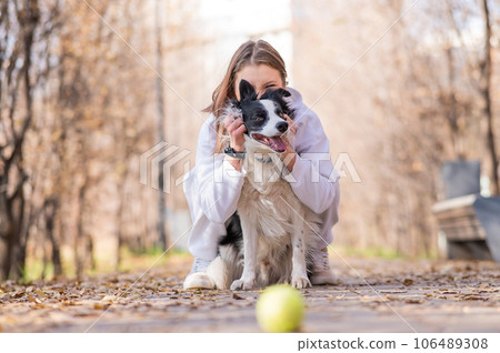 Caucasian woman hugging her dog on a walk in the autumn park. Border collie looks at the ball. 106489308