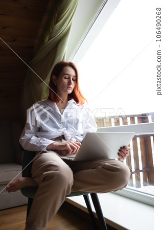 young beautiful woman working at a laptop sitting by a large window. remote work concept young beautiful woman working at a laptop sitting by a large window. remote work concept 106490268