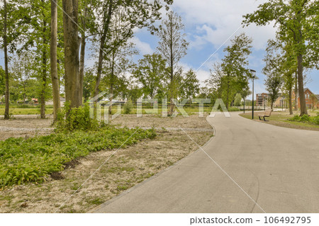 an empty street in the middle of a residential area with lots of trees and bushes on either side of the road 106492795