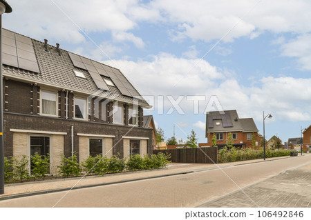 an empty street with houses in the background and a blue sky above it, as seen from across the street 106492846