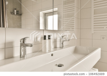 a modern bathroom with white tile walls and counter space for soaps, hand washers and other items on the sink is in 106492889