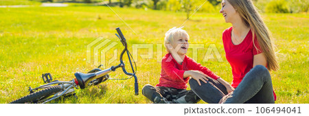 Mom and son rest on the lawn after riding a bike BANNER, LONG FORMAT 106494041