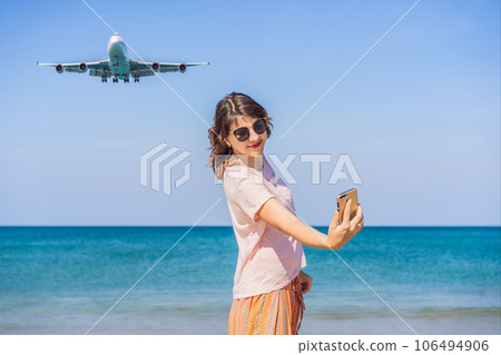 Woman makes a selfie on the beach watching the landing planes. Traveling on an airplane concept. Text space. Island Phuket in Thailand. Impressive paradise. Hot beach Mai Khao. Amazing landscape Woman makes a selfie on the beach watching the landing planes. Traveling on an airplane concept. Text space. Island Phuket in Thailand. Impressive paradise. Hot beach Mai Khao. Amazing landscape 106494906