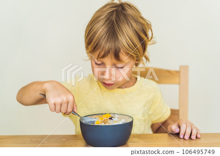 Happy boy sitting and eating a fresh smoothie bowl with mango, dragon fruit, granola and chia seeds Happy boy sitting and eating a fresh smoothie bowl with mango, dragon fruit, granola and chia seeds 106495749