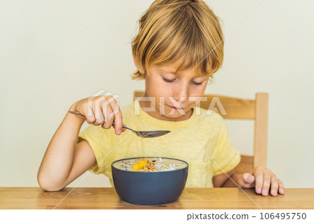 Happy boy sitting and eating a fresh smoothie bowl with mango, dragon fruit, granola and chia seeds 106495750