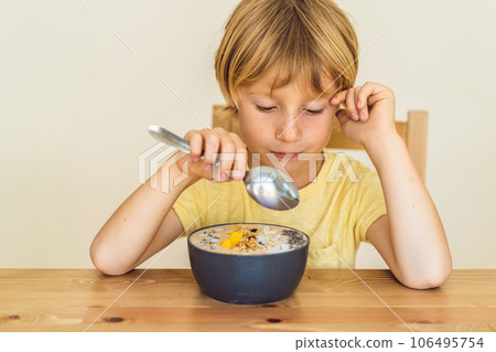 Happy boy sitting and eating a fresh smoothie bowl with mango, dragon fruit, granola and chia seeds 106495754
