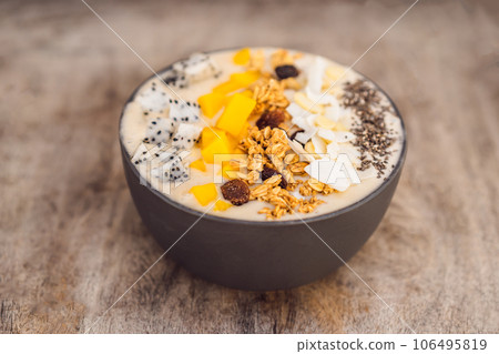 Smoothie bowls made with mango, banana, granola, grated coconut, dragon fruit, chia seeds and mint on wooden background. Concept fruits, vitamins Smoothie bowls made with mango, banana, granola, grated coconut, dragon fruit, chia seeds and mint on wooden background. Concept fruits, vitamins 106495819