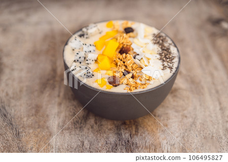 Smoothie bowls made with mango, banana, granola, grated coconut, dragon fruit, chia seeds and mint on wooden background. Concept fruits, vitamins Smoothie bowls made with mango, banana, granola, grated coconut, dragon fruit, chia seeds and mint on wooden background. Concept fruits, vitamins 106495827