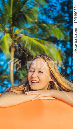 Summer lifestyle portrait of pretty girl sitting on the orange inflatable sofa on the beach of tropical island. Relaxing and enjoying life on air bed VERTICAL FORMAT for Instagram mobile story or Summer lifestyle portrait of pretty girl sitting on the orange inflatable sofa on the beach of tropical island. Relaxing and enjoying life on air bed VERTICAL FORMAT for Instagram mobile story or 106496894