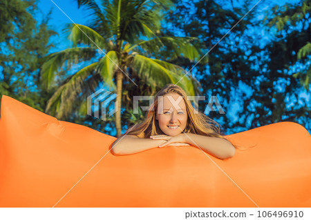 Summer lifestyle portrait of pretty girl sitting on the orange inflatable sofa on the beach of tropical island. Relaxing and enjoying life on air bed Summer lifestyle portrait of pretty girl sitting on the orange inflatable sofa on the beach of tropical island. Relaxing and enjoying life on air bed 106496910