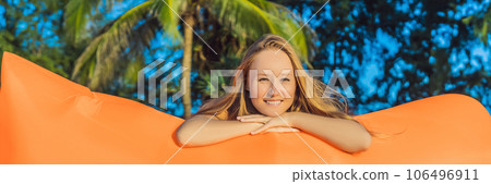 Summer lifestyle portrait of pretty girl sitting on the orange inflatable sofa on the beach of tropical island. Relaxing and enjoying life on air bed BANNER, LONG FORMAT 106496911