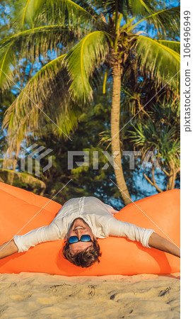 Summer lifestyle portrait of man sitting on the orange inflatable sofa on the beach of tropical island. Relaxing and enjoying life on air bed VERTICAL FORMAT for Instagram mobile story or stories size Summer lifestyle portrait of man sitting on the orange inflatable sofa on the beach of tropical island. Relaxing and enjoying life on air bed VERTICAL FORMAT for Instagram mobile story or stories size 106496949