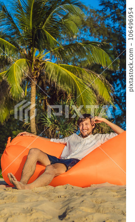 Summer lifestyle portrait of man sitting on the orange inflatable sofa on the beach of tropical island. Relaxing and enjoying life on air bed VERTICAL FORMAT for Instagram mobile story or stories size 106496954