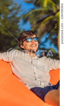 Summer lifestyle portrait of man sitting on the orange inflatable sofa on the beach of tropical island. Relaxing and enjoying life on air bed VERTICAL FORMAT for Instagram mobile story or stories size Summer lifestyle portrait of man sitting on the orange inflatable sofa on the beach of tropical island. Relaxing and enjoying life on air bed VERTICAL FORMAT for Instagram mobile story or stories size 106496968