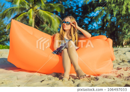 Summer lifestyle portrait of pretty girl sitting on the orange inflatable sofa on the beach of tropical island. Relaxing and enjoying life on air bed Summer lifestyle portrait of pretty girl sitting on the orange inflatable sofa on the beach of tropical island. Relaxing and enjoying life on air bed 106497033