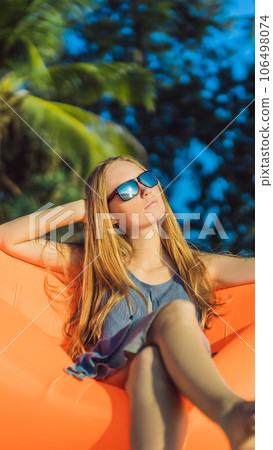 Summer lifestyle portrait of pretty girl sitting on the orange inflatable sofa on the beach of tropical island. Relaxing and enjoying life on air bed VERTICAL FORMAT for Instagram mobile story or Summer lifestyle portrait of pretty girl sitting on the orange inflatable sofa on the beach of tropical island. Relaxing and enjoying life on air bed VERTICAL FORMAT for Instagram mobile story or 106498074