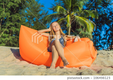Summer lifestyle portrait of pretty girl sitting on the orange inflatable sofa on the beach of tropical island. Relaxing and enjoying life on air bed Summer lifestyle portrait of pretty girl sitting on the orange inflatable sofa on the beach of tropical island. Relaxing and enjoying life on air bed 106498123