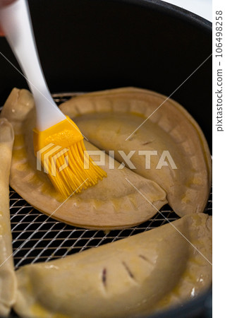 Brushing uncooked sweet cherry empanadas with egg wash to cook on the air fryer. 106498258