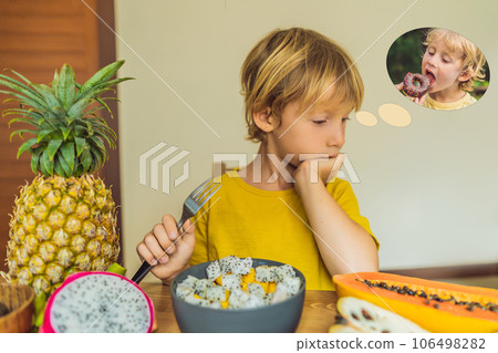Boy eats fruit but dreams about donuts. Harmful and healthy food for children. Child eating healthy snack. Vegetarian nutrition for kids. Vitamins for children. Junk food concept 106498282