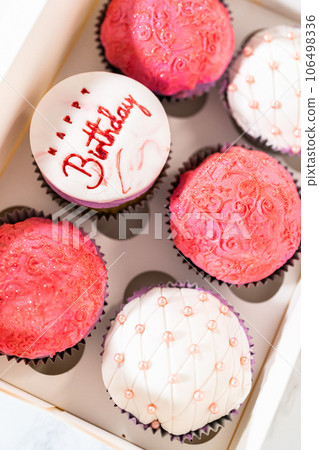 The birthday cupcakes, beautifully embellished with fondant decorations, are being carefully placed into white paper boxes, ready for their grand presentation. The birthday cupcakes, beautifully embellished with fondant decorations, are being carefully placed into white paper boxes, ready for their grand presentation. 106498336