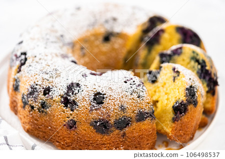 Slicing freshly baked lemon blueberry bundt cake with powdered sugar dusting. Slicing freshly baked lemon blueberry bundt cake with powdered sugar dusting. 106498537